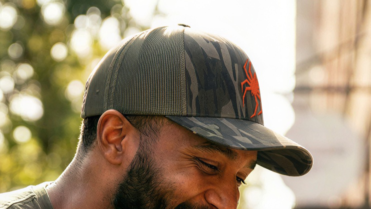 Man sitting outdoors holding a coffee cup, wearing a cap and casual clothing.